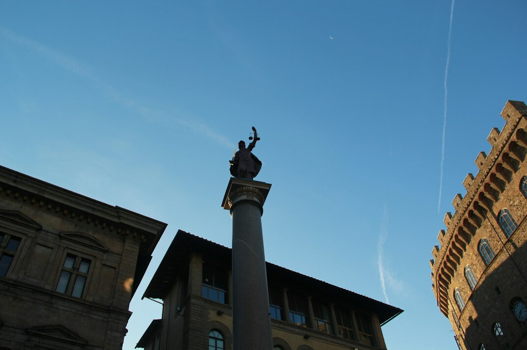 Monument column with a statue beside historic buildings